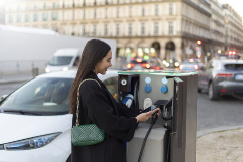 femme qui recharge sa voiture électrique sur une borne de recharge en ville