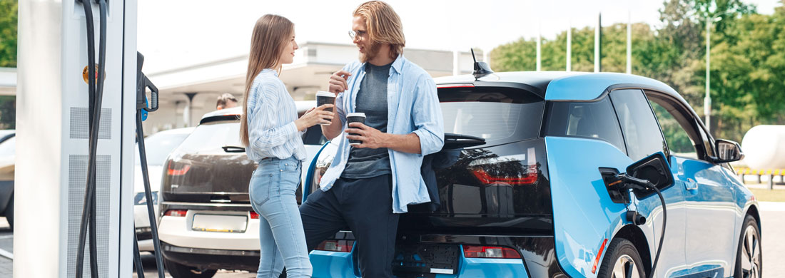 couple discutant pendant que la voiture électrique charge sur une borne de recharge sur un parking