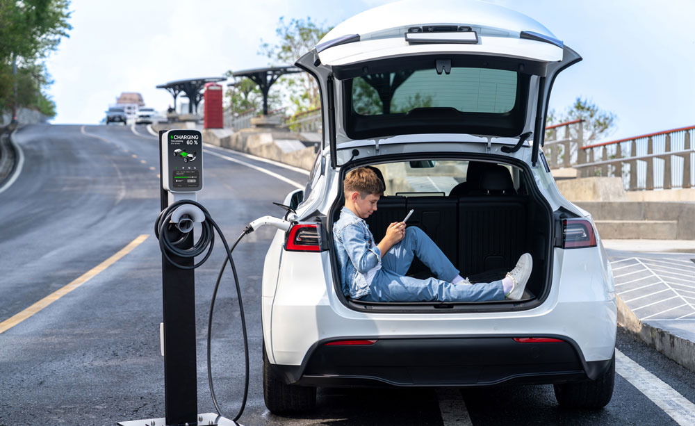 enfant dan coffre ouvert d'une voiture électrique. Le véhicule électrique se recharge sur une borne de recharge