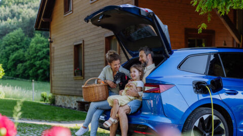 famille assise dans le coffre d'une voiture électrique. La voiture électrique charge sur une borne de recharge