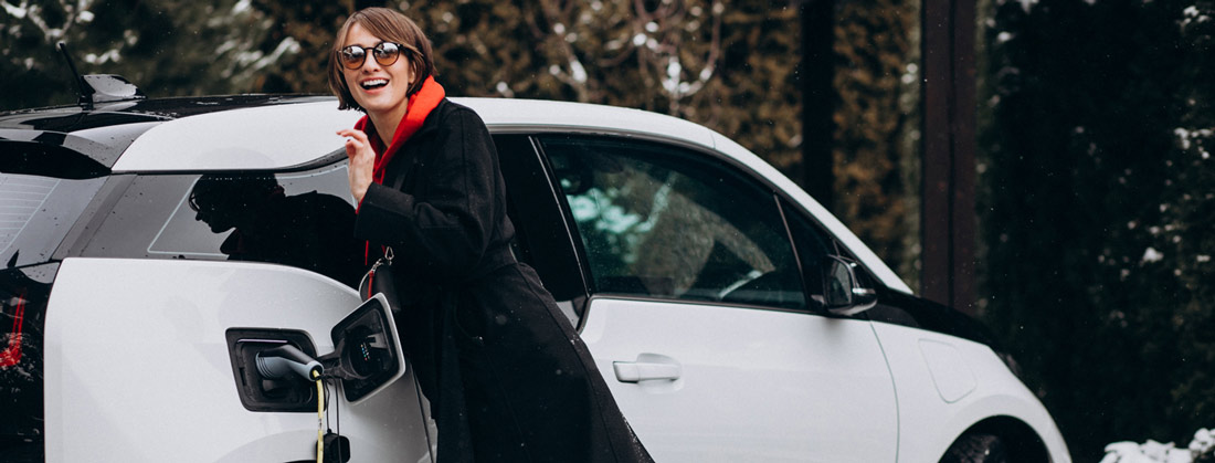 femme souriante recharge sz voiture électrique, plan sur la prise électrique