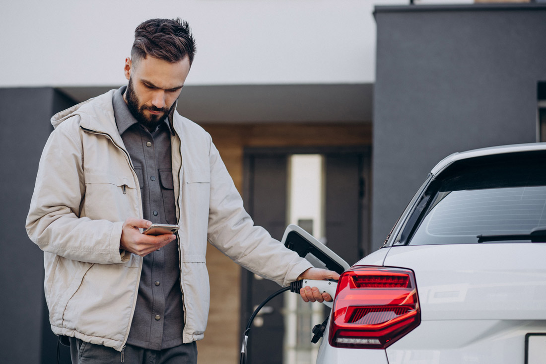 homme regarde son téléphone pendant que sa voiture électrique charge sur borne de echarge