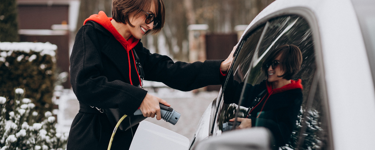 femme recharge sa voiture electrique dans la neige pendant les vacances de noel